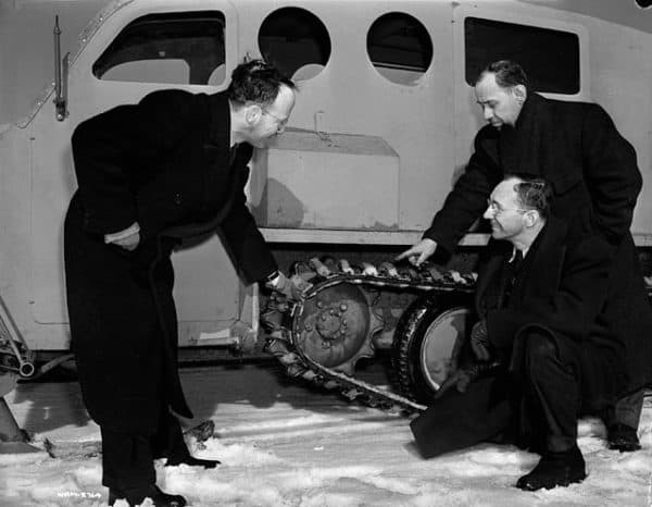 March, 1943: Armand Bombardier explains the construction of the Bombardier military snowmobile's track to two men.  (Credit: National Film Board of Canada. Photothèque / Library and Archives Canada)